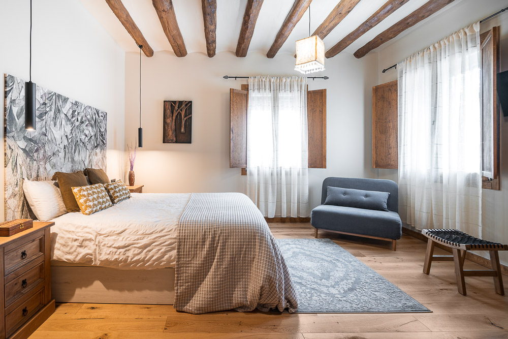 Dormitorio principal con vigas de madera vistas y cabecero decorativo - reforma rural en Navarra