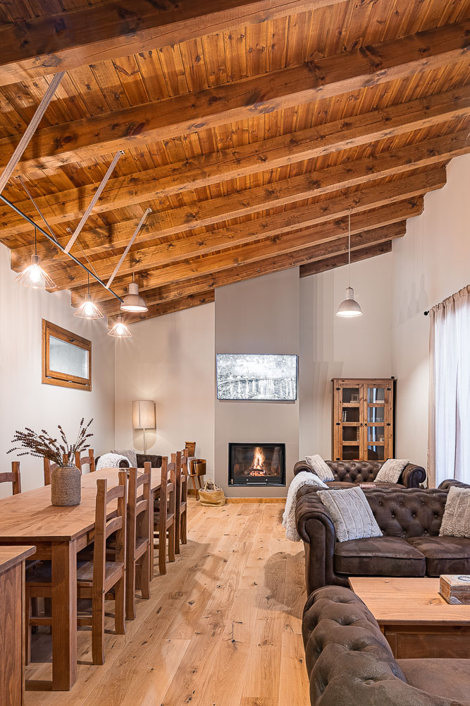 Vista del salón comedor con chimenea encendida y estructura de madera vista