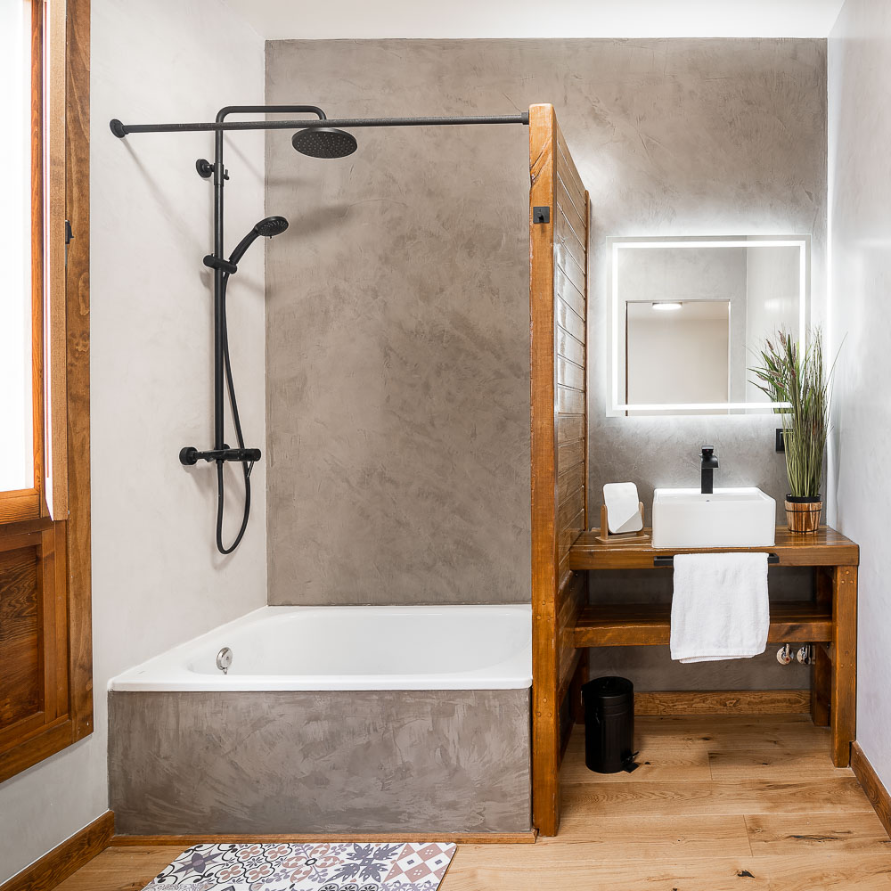 Baño rústico con bañera, mampara de madera y revestimiento en microcemento