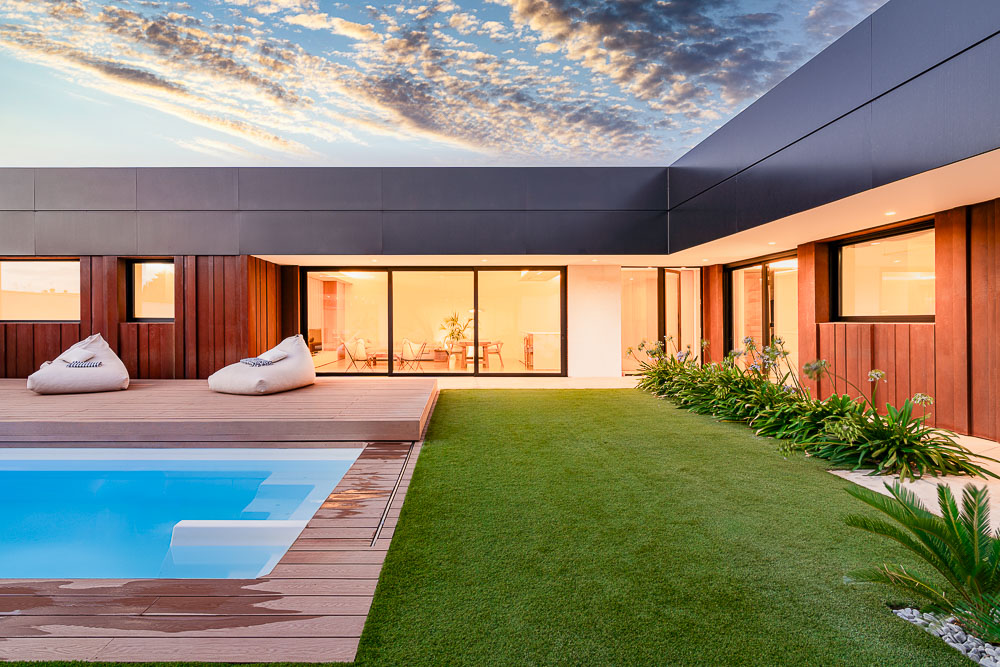Piscina con deck de madera y fachada de vivienda al atardecer - proyecto Arquitectura de la Ribera