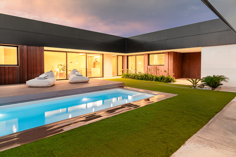 Piscina iluminada al anochecer con fachada de madera y acero corten - Casa Silis