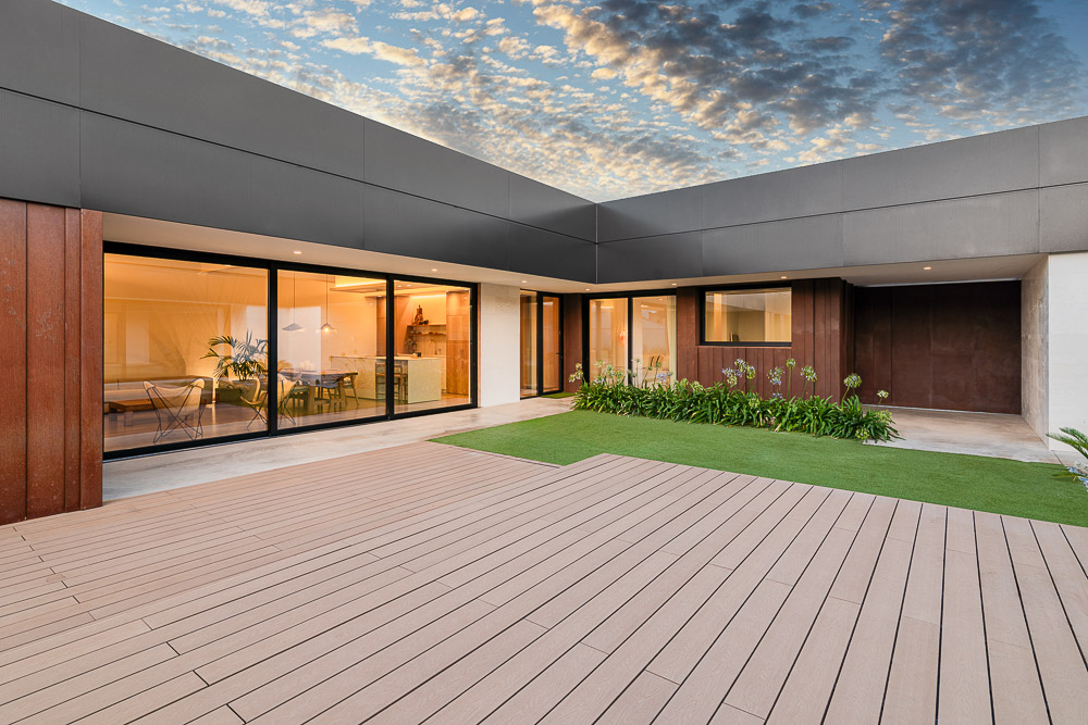 Vista exterior nocturna de vivienda con fachada de madera y jardín - Arquitectura de la Ribera