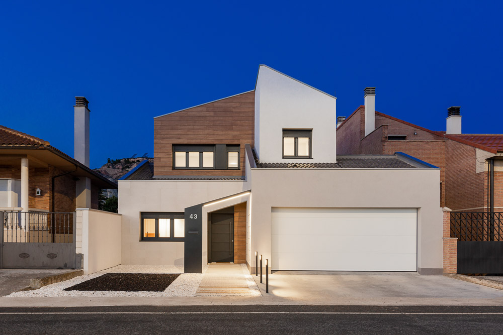 Fachada nocturna de vivienda unifamiliar moderna con madera y garaje - Casa Tilio, Arquitectura de la Ribera