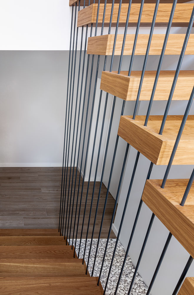 Detalle de escalera de madera con barandilla metálica vertical - Casa Tilio