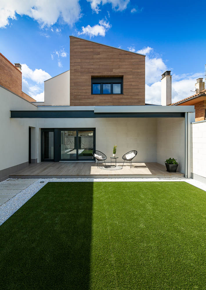 Vista de fachada trasera con revestimiento de madera y terraza cubierta - Casa Tilio