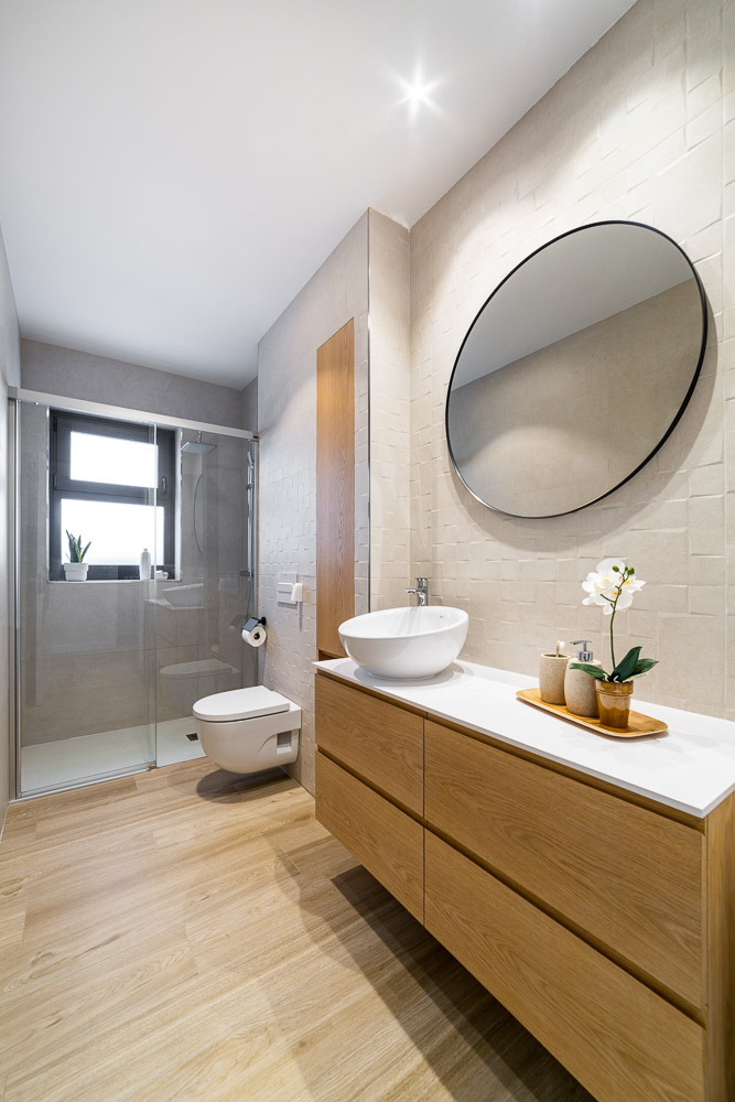 Baño con mueble de madera, espejo redondo y ducha con mampara - Casa Tilio, Arquitectura de la Ribera