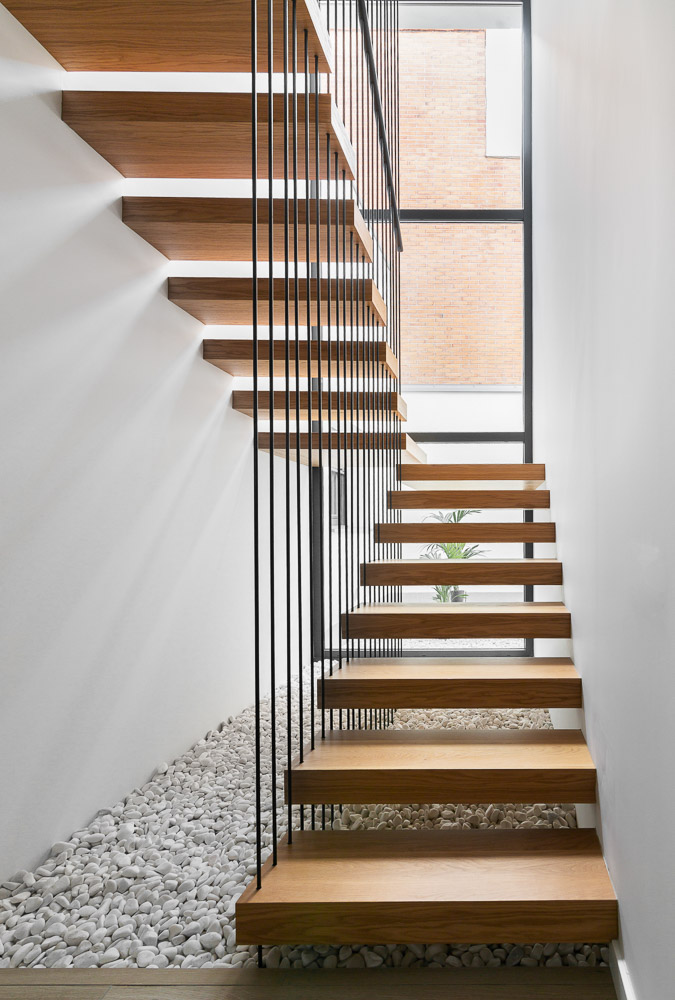 Vista de escalera interior con peldaños de madera y patio de luces - Casa Tilio