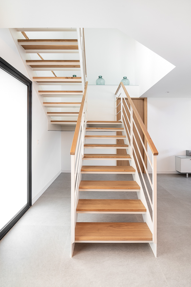 Escalera abierta con huellas de madera y gran ventanal, arquitectura e interiorismo de vivienda en Corella, Navarra
