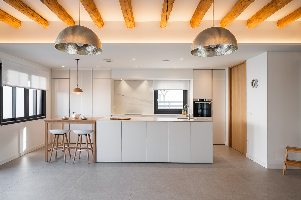 Cocina abierta con isla blanca y techo de vigas de madera vista, interiorismo de vivienda en Corella, Navarra