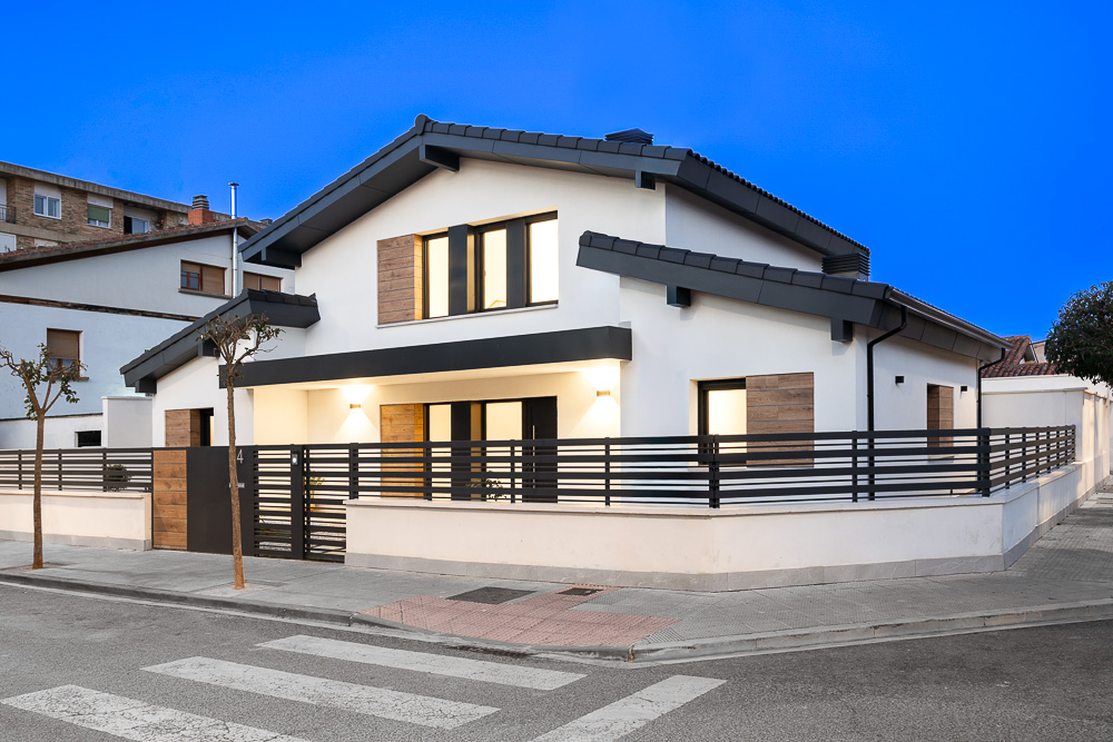 Fachada principal iluminada al anochecer en esquina, vivienda unifamiliar diseñada por arquitecto en Navarra
