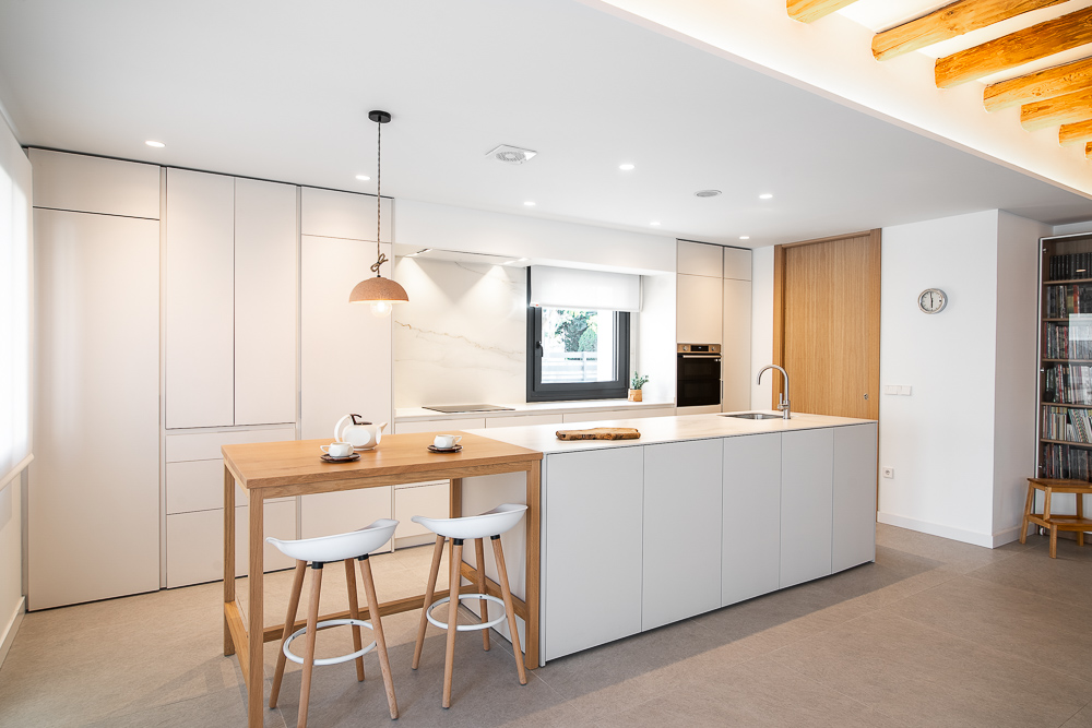 Cocina blanca con armarios hasta el techo y barra de madera con taburetes, diseño de Arquitectura de la Ribera