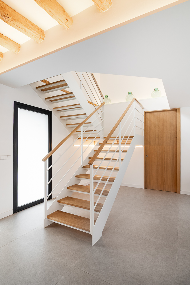 Escalera con barandilla metálica y pasamanos de madera junto a ventanal negro, diseño de arquitecto en Corella