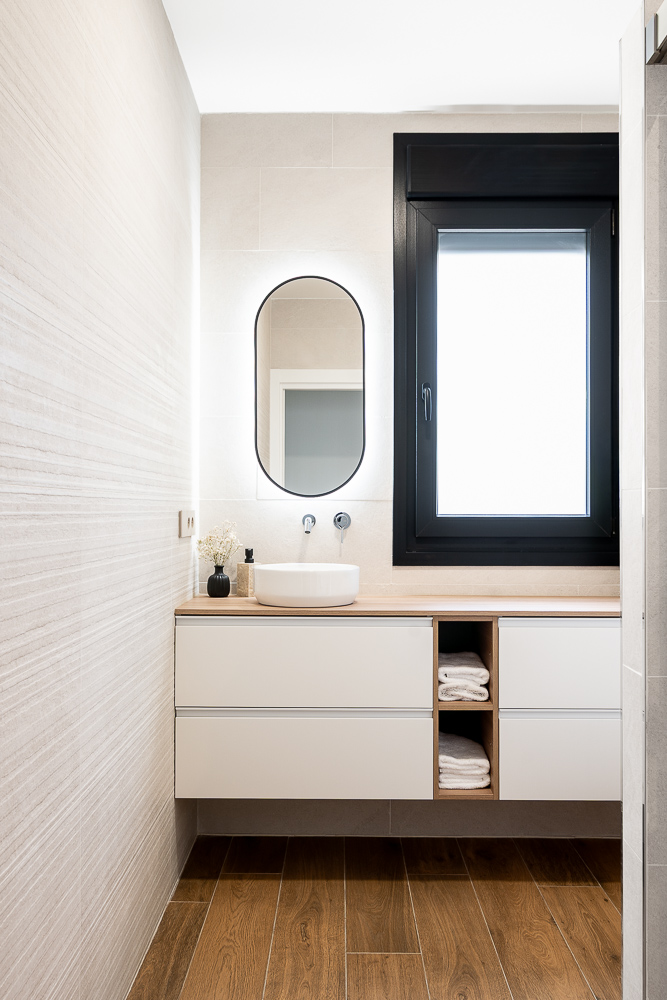 Baño con espejo ovalado retroiluminado y mueble suspendido blanco, interiorismo de vivienda en Cintruénigo, Navarra