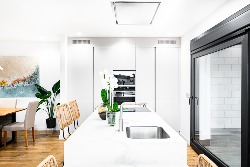 Cocina blanca con hornos integrados e isla con fregadero, diseño de arquitecto en Navarra