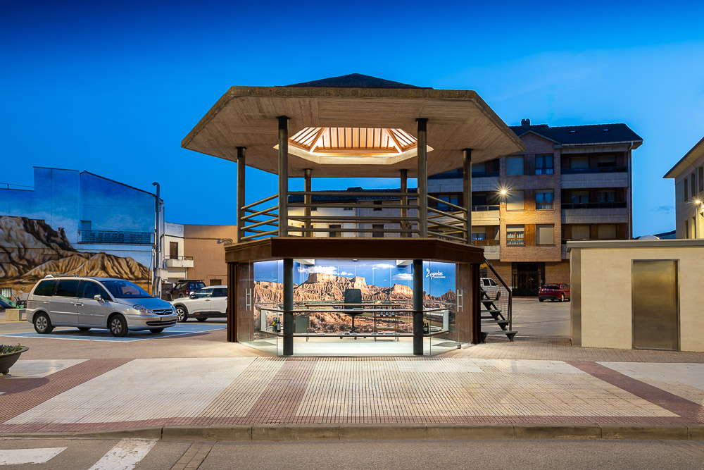 Vista nocturna del centro de información con planta baja acristalada y mural de las Bardenas, obra de Arquitectura de la Ribera en Arguedas