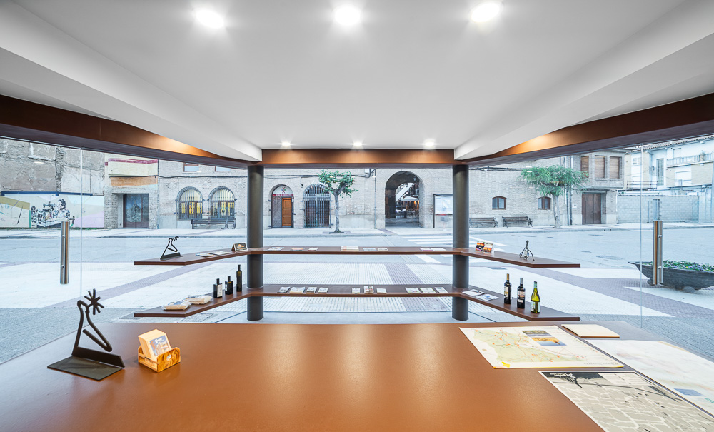 Vista desde el interior acristalado hacia la plaza, con baldas de madera para productos locales, arquitectura de Arquitectura de la Ribera